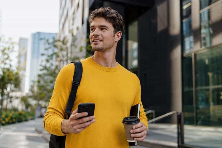 A Bolt Affiliate holding a phone and coffee while walking through the city
